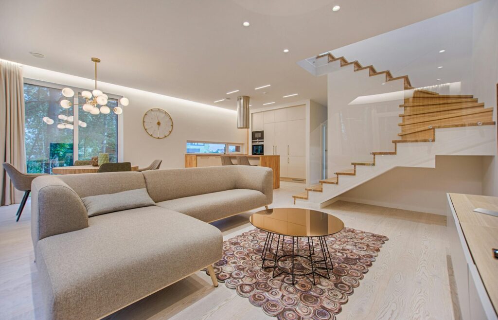 Contemporary living room with neutral tones, a sleek sofa, and elegant wooden staircase. second home management Spain