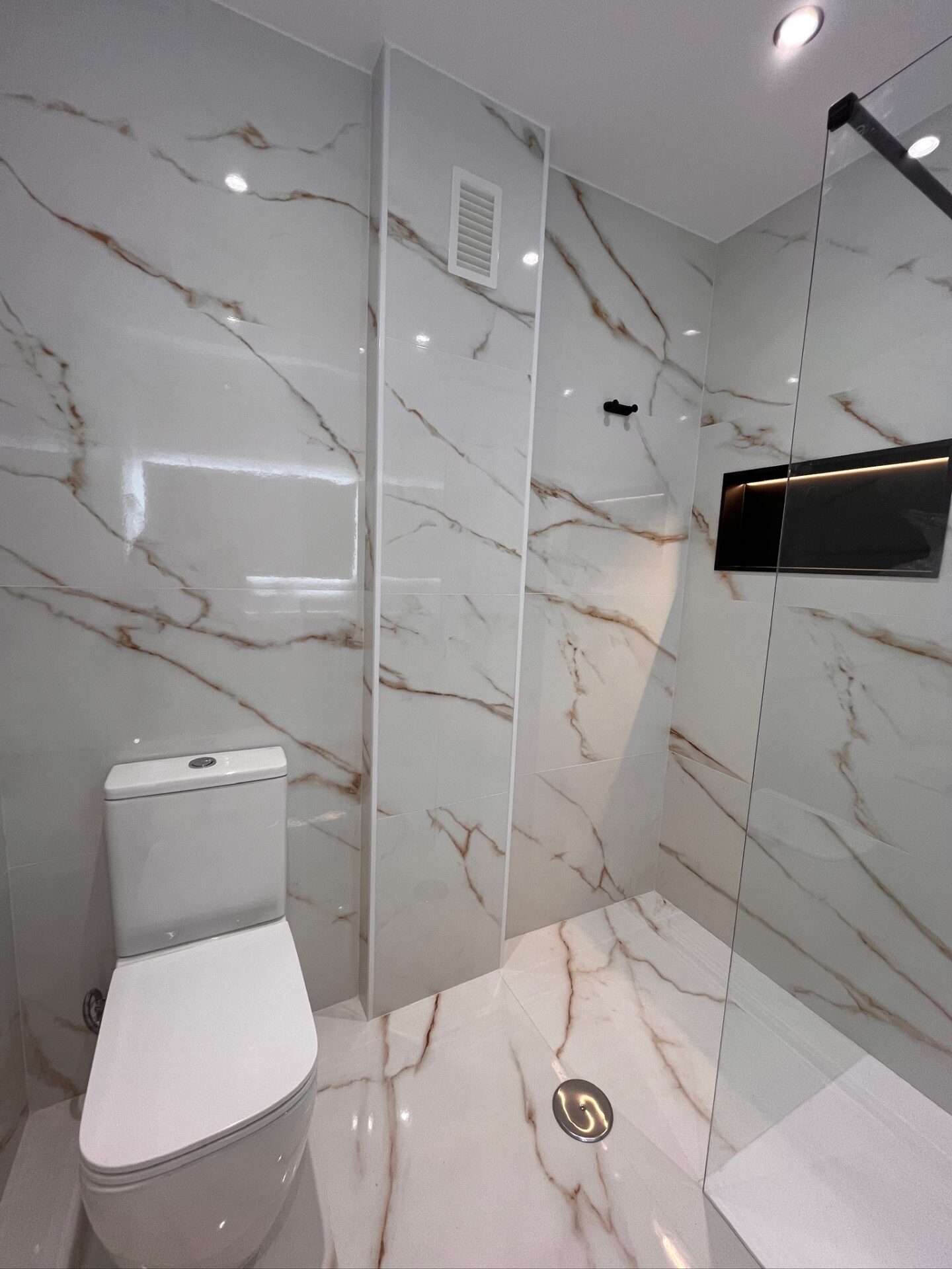 Finished bathroom detail with marble-look wall tiles, toilet and glass shower screen